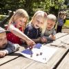 Fire børnehavebørn spiller sneglestafet på en bænk ved børnehusets legeplads