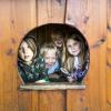 Fire børn kigger smilende ud fra rundt vindue i legehus