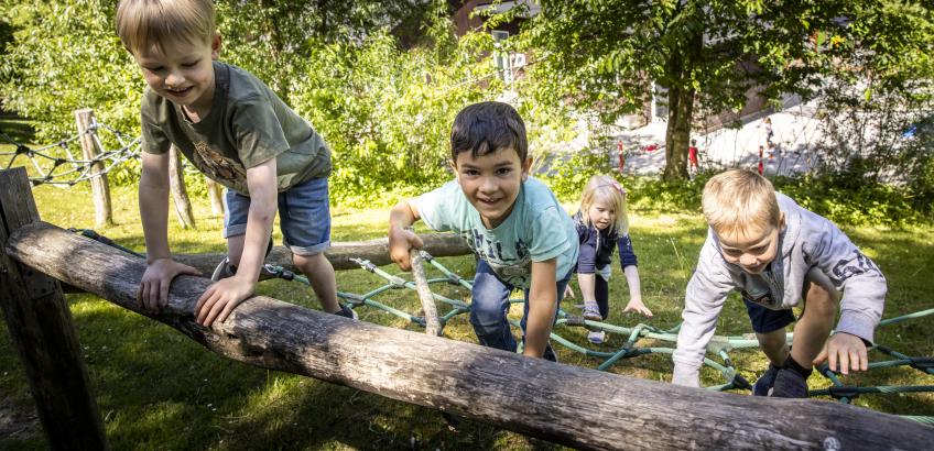 Fire børnehavebørn klatrer op af klatrestativ i børnehaven