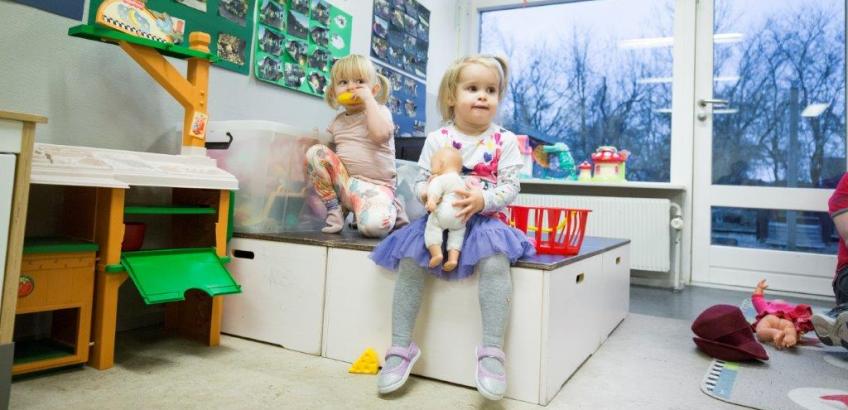 Børn sidder på bænk i et af børnehusets legerum