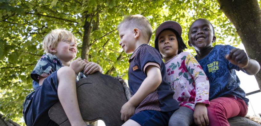 Fire glade børn i børnehaven leger på en træhest