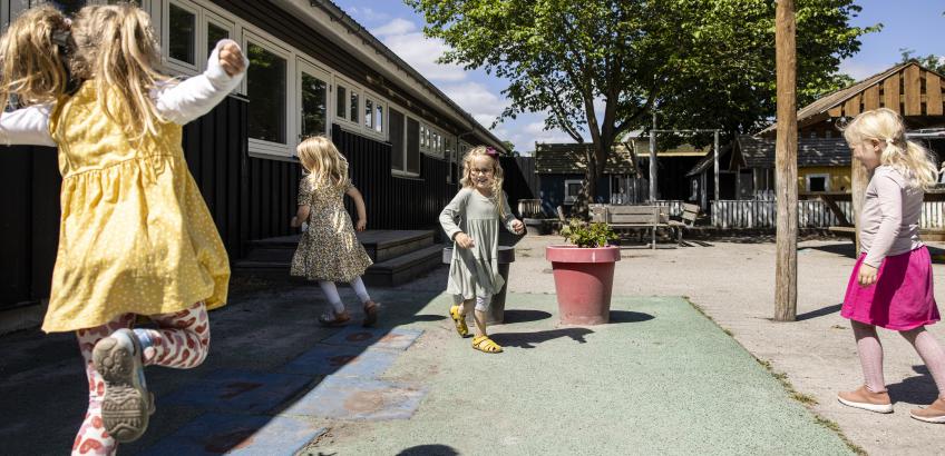 Fire glade børnehavebørn hinker på børnehuset legeplads