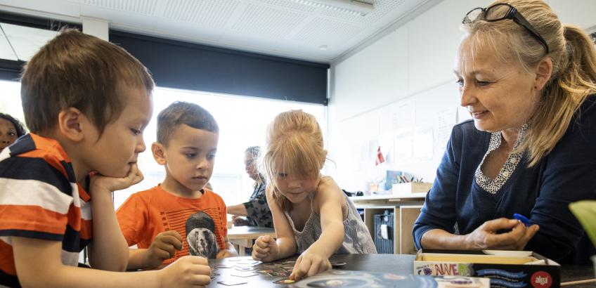 Pædagog spiller spil med tre børn i børnehaven