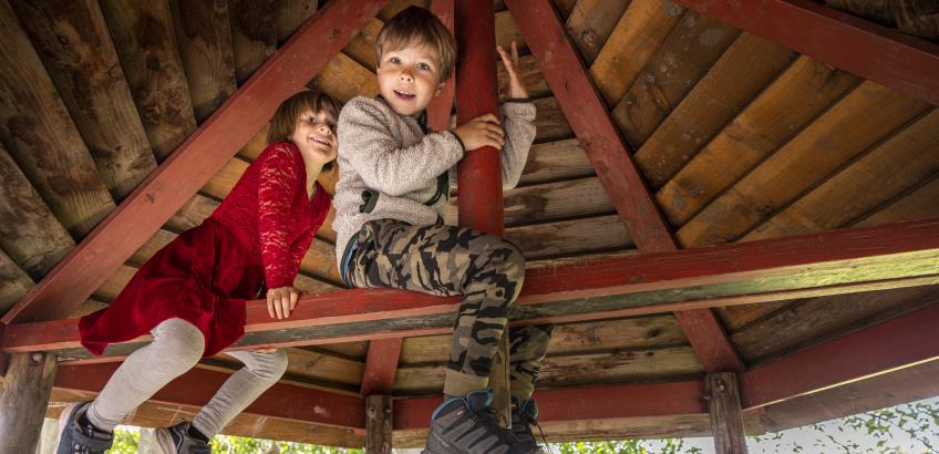 To børn sidder på en rød bjælke i børnehusets vingeslag