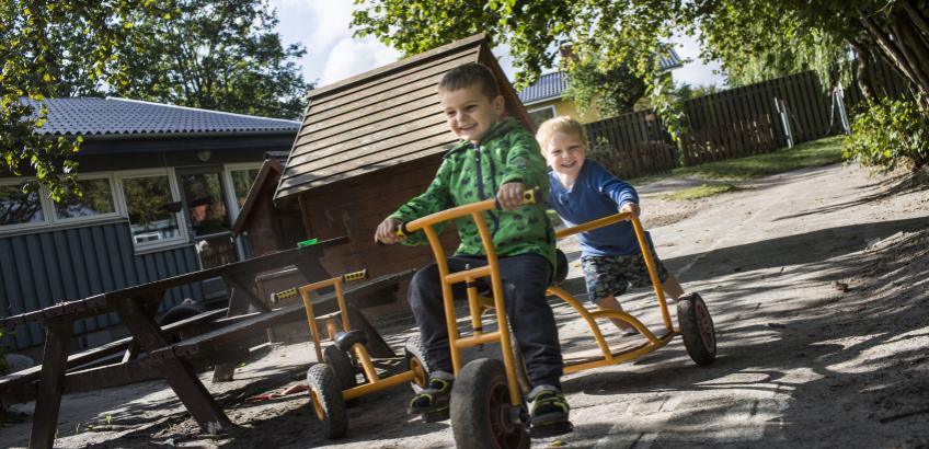 To drenge fra børnehaven leger sammen på en cykel i børnehuset
