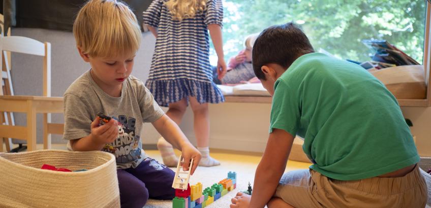 Børn leger med lego på en af stuerne i Troldebo og slapper af på bænken i vindueskarmen.